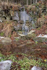 A small leafy pond with water flowing over stones.