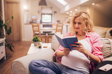 Pregnant woman sitting on a cozy chair and reading a book at home