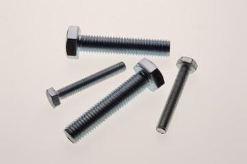 New, chrome-plated bolts and nuts of different sizes lie on a white background. Close-up