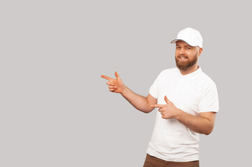 Bearded man wearing white cap and t shirt points aside at the grey copy space.
