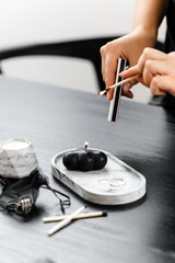 Handmade black figurative candle in a modern style, beautifully shaped.  Home decor, concrete stand on black table. A hand with a match lights the candle. Beautiful long matches. 