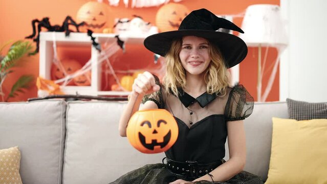 Young blonde woman wearing halloween costume holding pumpkin basket at home
