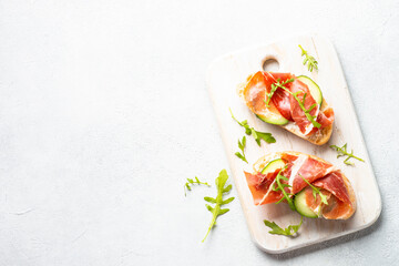 Open sandwiches with cream cheese, prosciutto and arugula at white background. Top view with copy space.