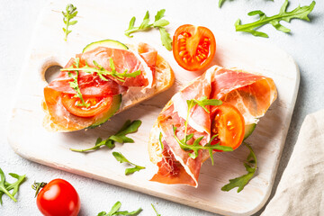 Open sandwiches with cream cheese, prosciutto and arugula at white background. Top view image.