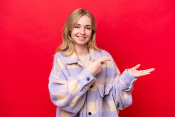 Young English woman isolated on red background holding copyspace imaginary on the palm to insert an...