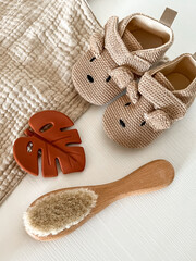 baby shoes, a baby hair brush, a rodent-leaf monster and a beige muslin scarf lie on a white...