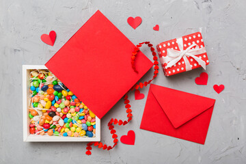 Red envelope with candy and gift box and Valentines hearts on colored background. Flat lay, top...