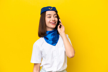 Airplane stewardess Ukrainian woman isolated on yellow background keeping a conversation with the mobile phone