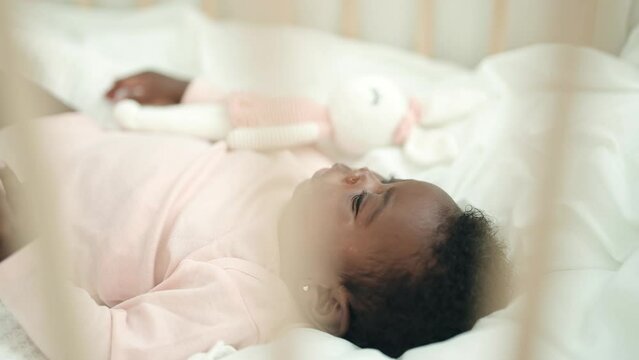 African american baby lying on cradle with relaxed expression at bedroom