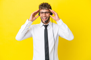 Telemarketer blonde man working with a headset isolated on yellow background with surprise expression