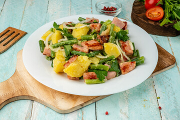 Liege salad of potatoes, bacon and beans in a white plate on a wooden board. A traditional dish....