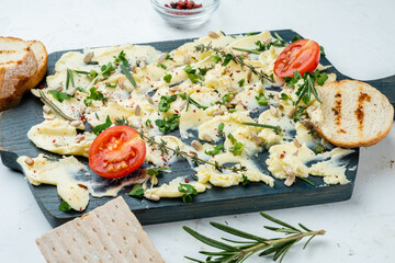 Delicious creamy butter snack with herbs and seeds, served on a wooden board with baguette and crackers, light background.