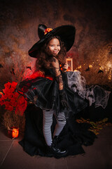 Naklejka premium Little girl in a witch's hat and black dress on the background of the cobwebs. Image for Halloween. Halloween costume