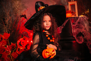 Little girl in a witch's hat and black dress on the background of the cobwebs. Image for Halloween. Halloween costume