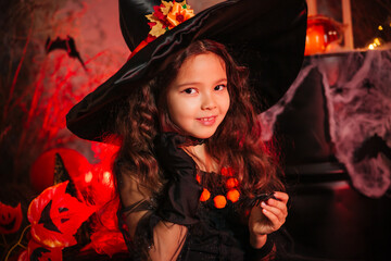 Little girl in a witch's hat and black dress on the background of the cobwebs. Image for Halloween. Halloween costume