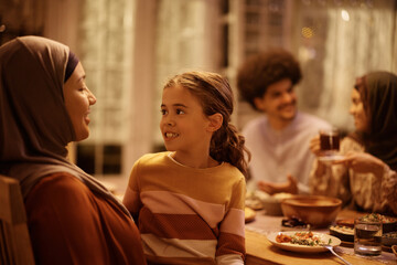 Small Muslim girl talks to her grandmother during family meal at dining table.
