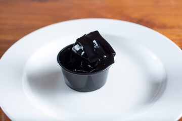 A view of a condiment cup of coffee jelly, on a plate.