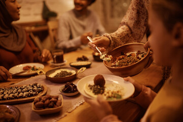 Close up of Muslim mother serving food to her daughter during family meal at dining table.