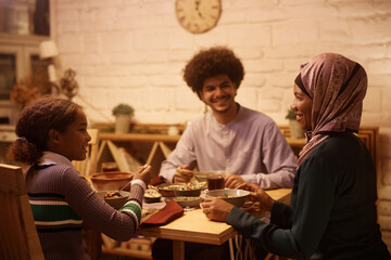 Fototapeta na wymiar Happy Muslim family enjoys in conversation while eating at dining table