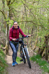 Fototapeta na wymiar Une cycliste à côté de son vélo avec le sourire dans les bois