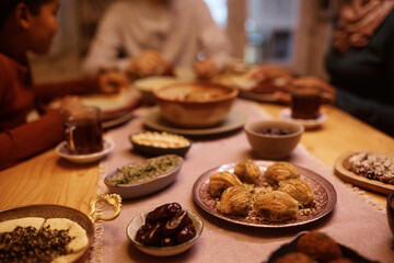 Close up of variety of food during Iftar meal on Ramadan with Muslim family in background.