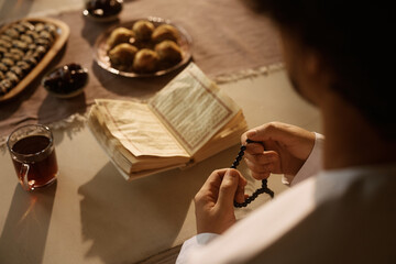Close up of Muslim man reads from Quran while using misbaha beads at dining table