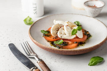 Caprese salad in modern feed with tomatoes, basil, mozzarella, pesto. Traditional Italian food with cutlery on white background, menu