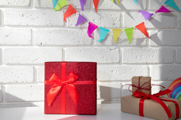 Shiny red gift with ribbon ties on a white background with a festive multi-colored garland