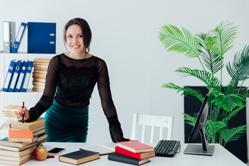 A business teacher stands at a table with a stack of books in the office