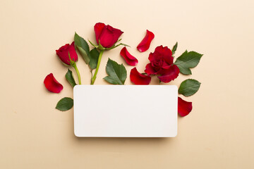 Greeting card mockup with red roses on color background, top view