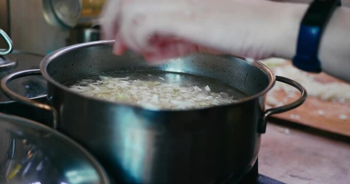 woman's hands throw sliced white cabbage into a steel pot of boiling broth, making homemade soup, selective focus