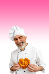 Baker man in love on valentine's day wearing chef's outfit. Chef-cooker in a chef's hat and jacket holding a heart-shaped muffin to his chest. Senior Character kitchener, pastry chef for advertising