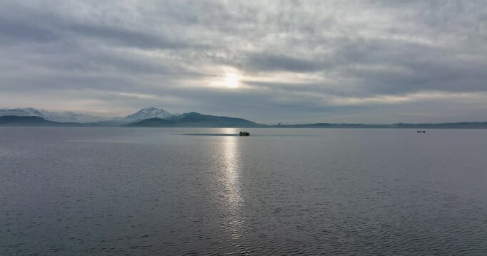 Aerial smooth arc shot of man alone in a tiny boat on a lake on a gloomy winter afternoon