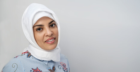 Portrait of middle-aged muslim woman wearing hijab head scarf over white background while looking at camera. face of cheerful woman covered with headscarf smiling. Casual islamic girl. Copy space - obrazy, fototapety, plakaty