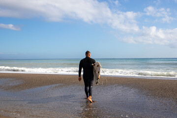 Surfer boy walking on the beach towards the sea to surf