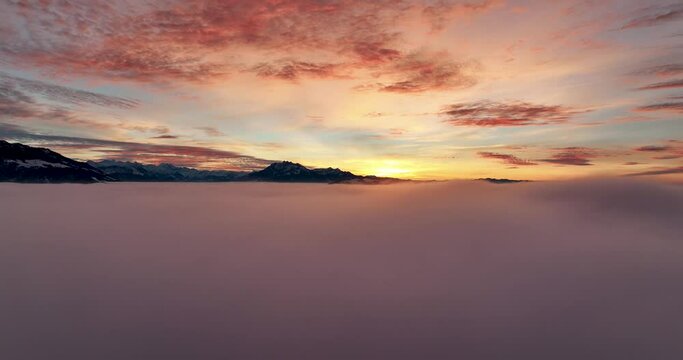 Aerial Tracking Shot flying over pink clouds towards snowy Swiss mountains at dawn