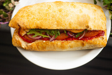 Large ciabatta sandwich with salad, fresh vegetables and onions, and meat.