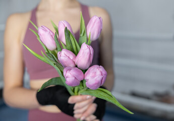 Girl boxer with bandaged hands holds seven tulips, women's sport, gentle boxing