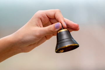 A small bell in the girl's hand on a neutral background, close-up, - obrazy, fototapety, plakaty