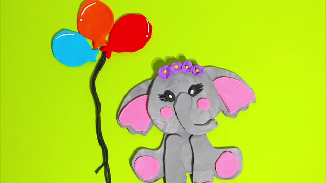 Cute elephant baby girl with a flower wreath on her head next to balloons. Stop motion animation. Concept of children's holiday, birthday, video card on a green background.