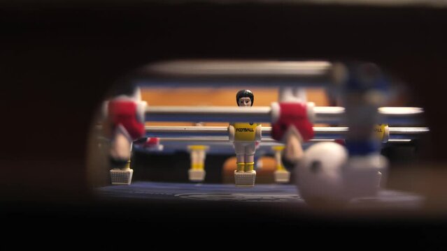 Close-up of foosball players figurines rotate during the game. People play mini foosball and score a goal with a ball into the goal. View from the football goal.