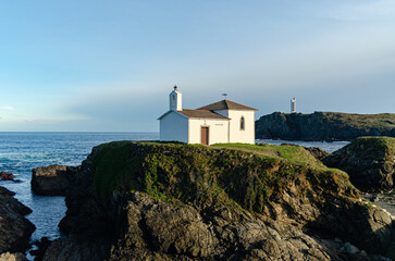 Fototapeta na wymiar Hermitage on some cliffs on the Galician coast, over the Atlantic Ocean with a blue sky and the Frouxeira lighthouse in the background.