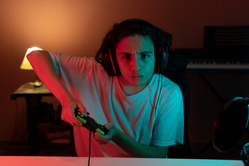 focused and concentrated gamer playing video games with a joystick at home with neon lights and microphone