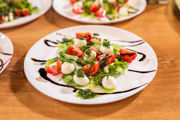 Plate of healthy classic close-up caprese salad with mozzarella cheese tomatoes and basil in kitchen - italian cuisine