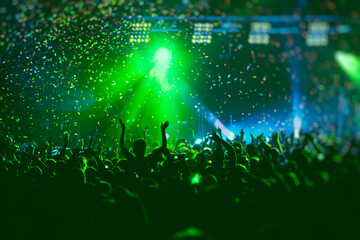 A crowded concert hall with scene stage green lights, rock show performance, with people silhouette, colourful confetti explosion fired on dance floor air during a concert festival