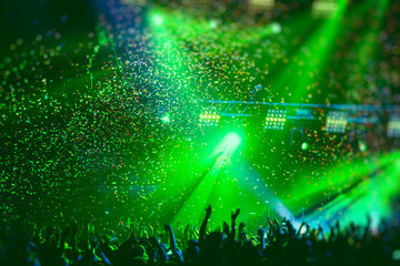 A crowded concert hall with scene stage green lights, rock show performance, with people silhouette, colourful confetti explosion fired on dance floor air during a concert festival