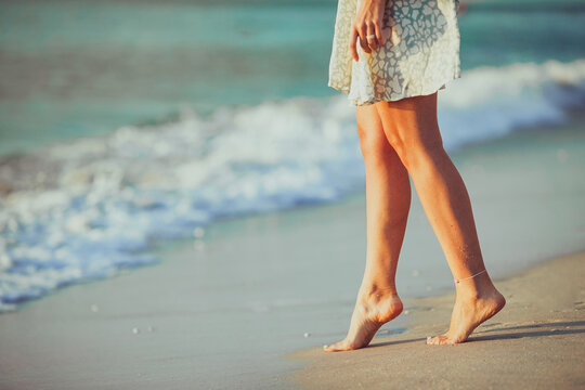 Female legs on the beach closeup. Woman in dress walking on the beach