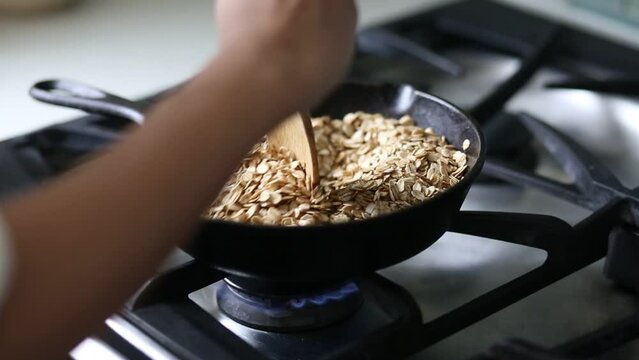 close up of woman's hand stirring oats toasting in cast iron skillet