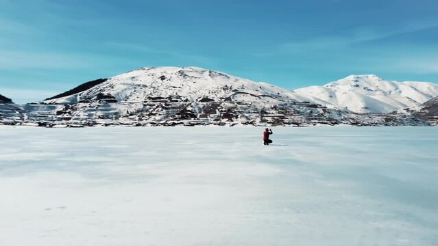 A man prostrates on the ground on the frozen lake. worship. Aerial View. Frozen lake, snowy mountains, trees, sunny sky.
