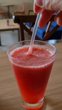 M&atilde;o mexendo suco de morango, suco de morango sendo tomado de canudinho.